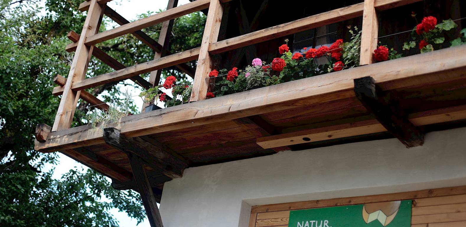 Balcone in legno con fiori rossi; sotto un'insegna con la scritta "Natur Sennerei Unterrüber".
