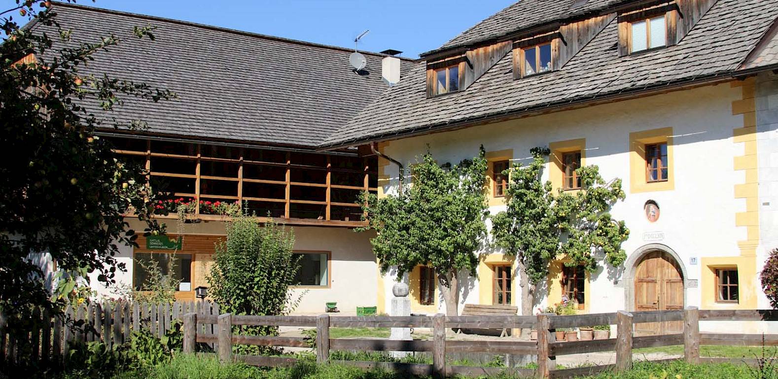 Una casa tradizionale a due piani con cornici gialle alle finestre, circondata da giardino e staccionata.
