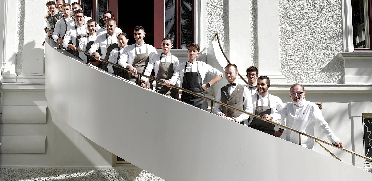 Eine Gruppe von Köchen in weißen Uniformen steht auf einer mit Holzstufen versehenen Treppe.