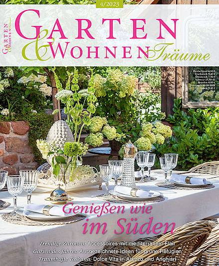 Gedeckter Tisch im sonnigen Garten mit Blumen; Zeitschriftentitel "Garten &amp; Wohnen Träume".