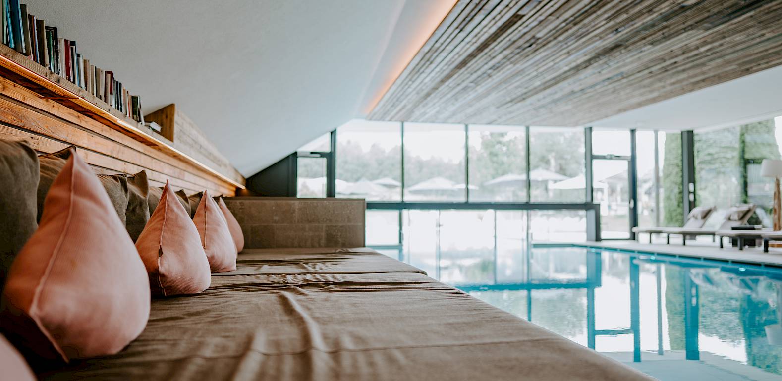 Interno accogliente con cuscini e vista su piscina coperta attraverso grandi finestre. Stile moderno.