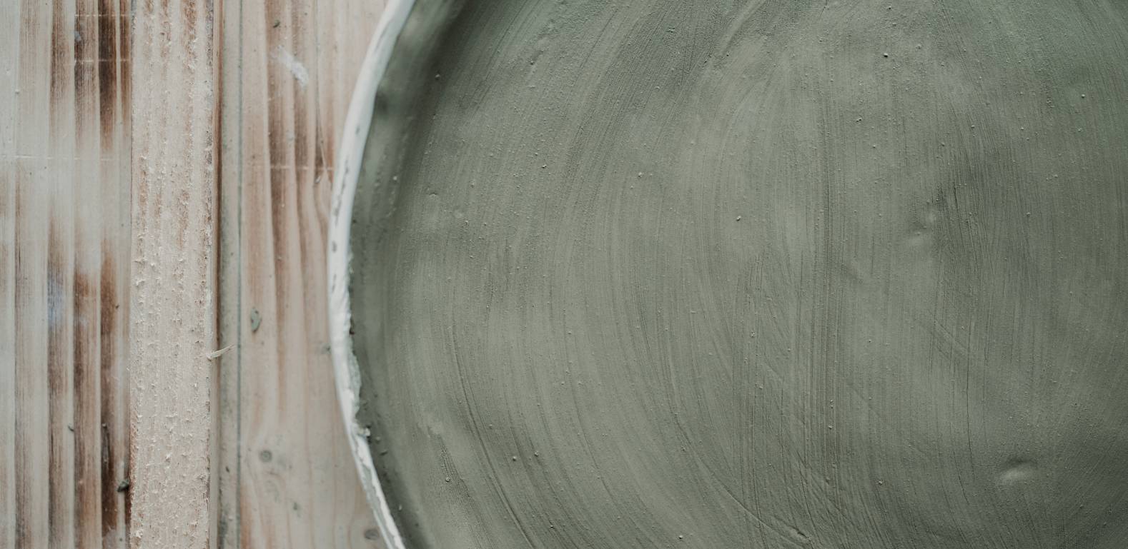 Keramikschale mit mattem, grünem Finish auf einem Holztisch, minimalistisch und schlicht dargestellt.
