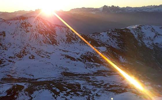 Sunrise over snowy mountains, with a frozen lake in the foreground.