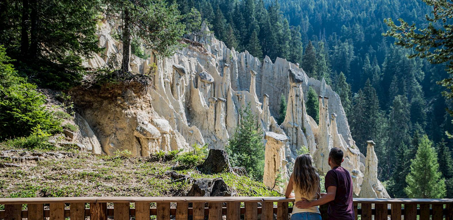 Ein Paar betrachtet beeindruckende Felsformationen in einer von Bäumen gesäumten Berglandschaft.