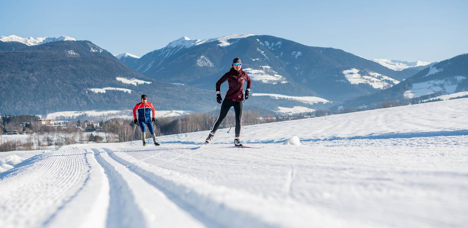 Langläufer in winterlicher Berglandschaft mit klarem Himmel. Im Vordergrund perfekt gespurte Loipen.